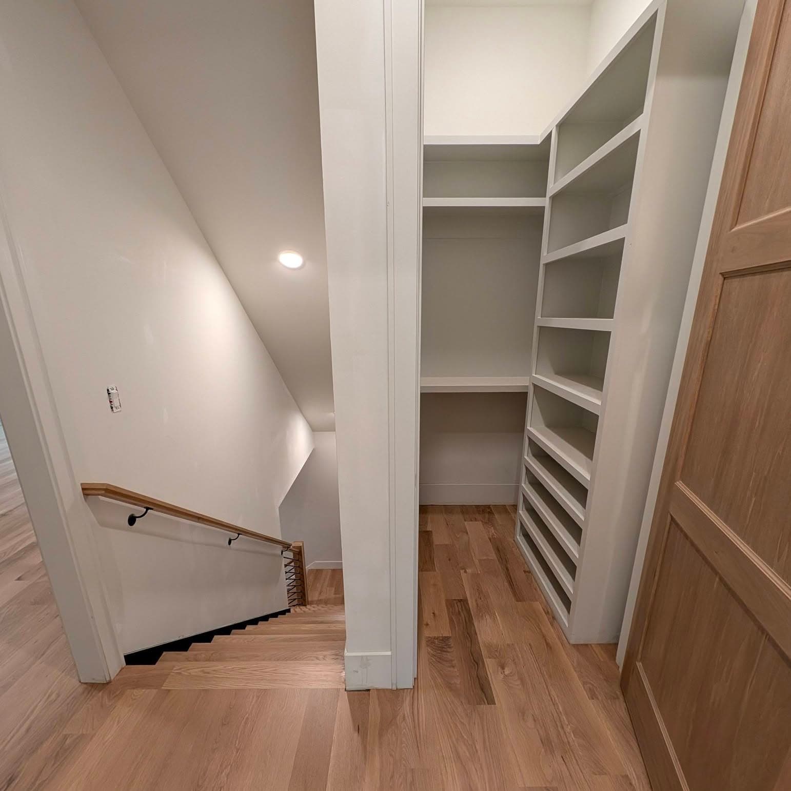 Stair with wood handrail descending past built-in shelving; refinished treads and landing