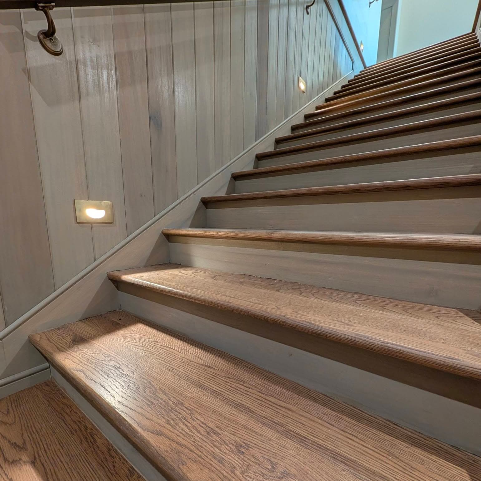 Stairs with glass panel railing, light oak treads, dark risers, downlights