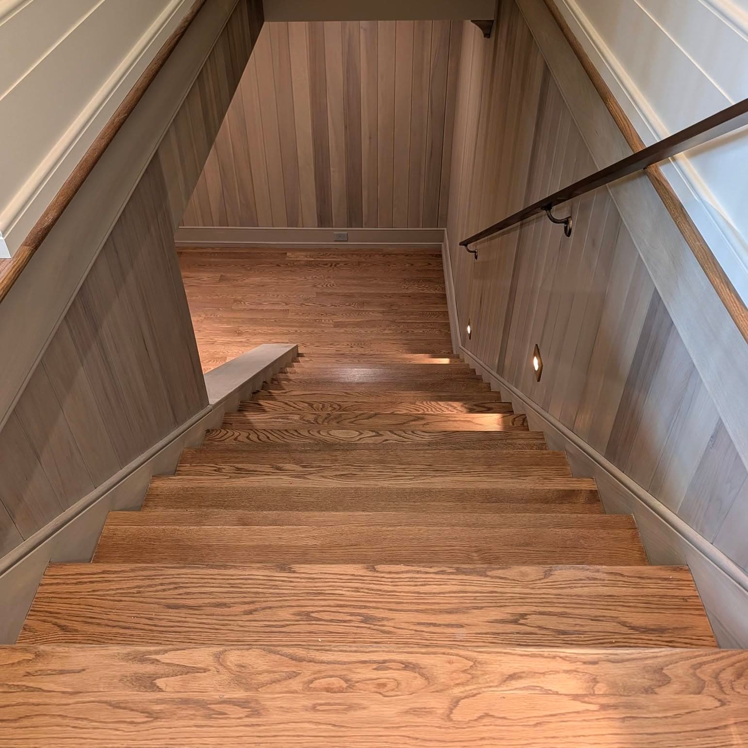 Straight stair run viewed from below, red oak treads and paneled wainscot walls