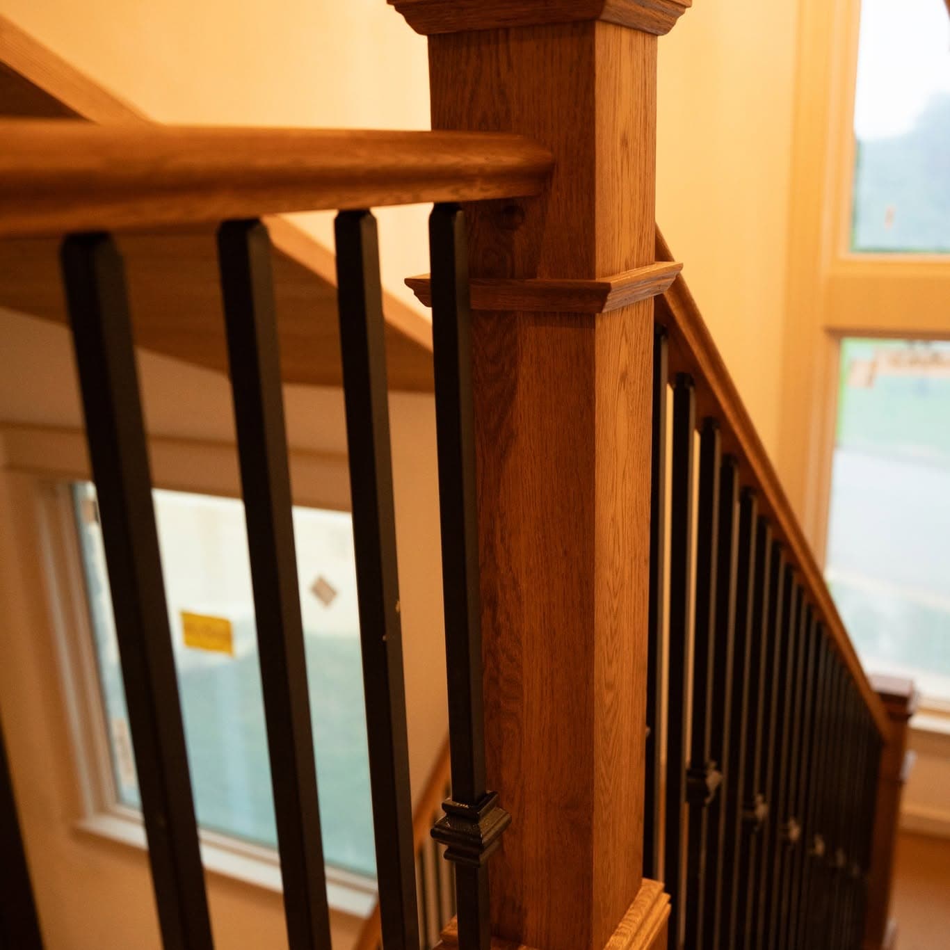 Close view of heavy square newel post and black balusters at stair base