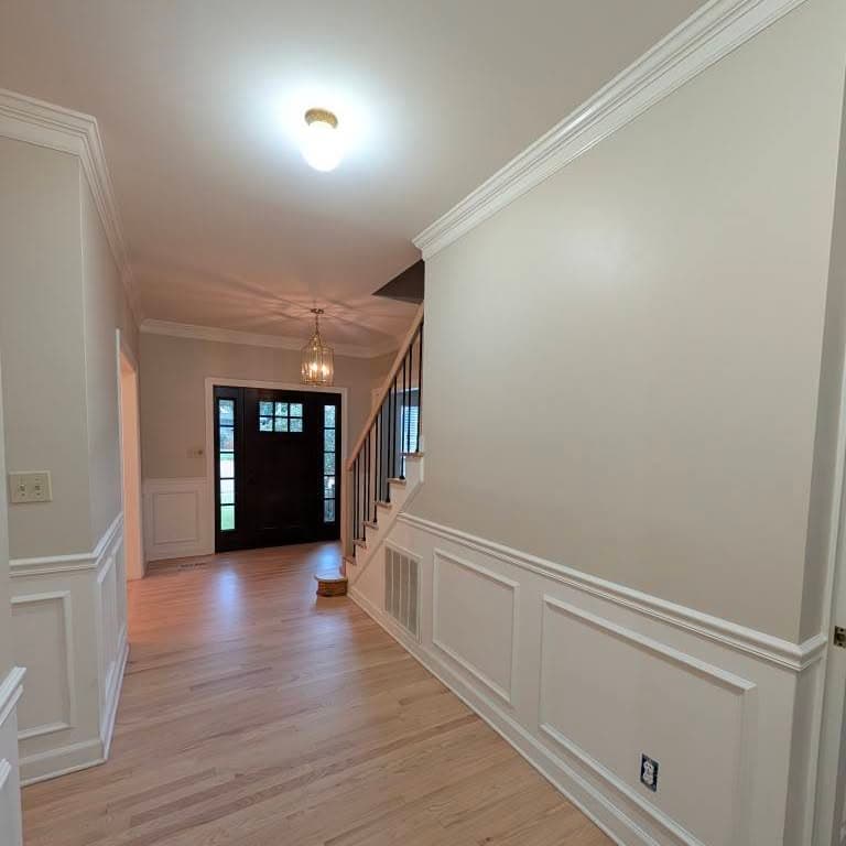 Hallway to entry with stair at right: light oak treads, white risers, black metal balusters
