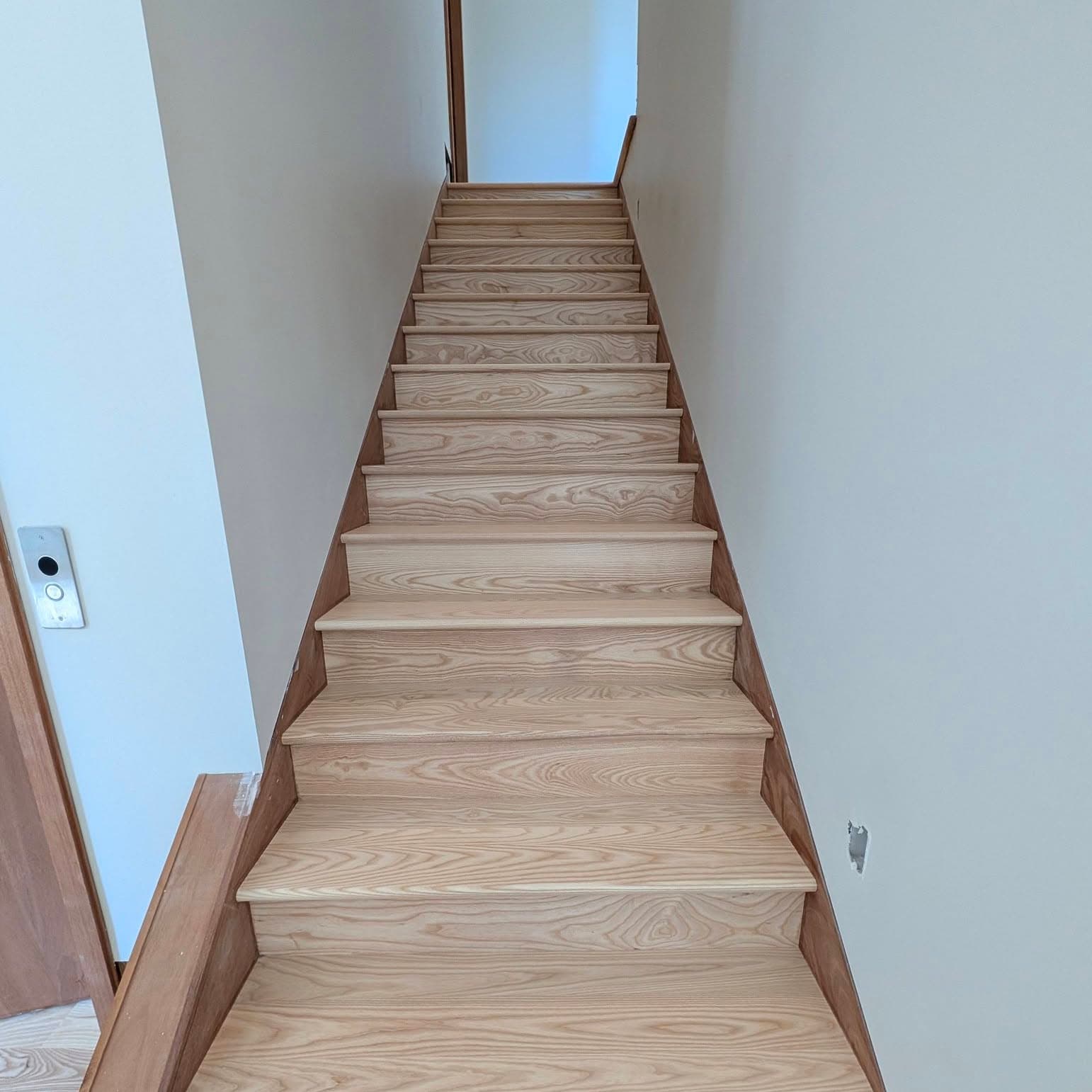 Looking up a light wood stair run in a narrow white-walled hall