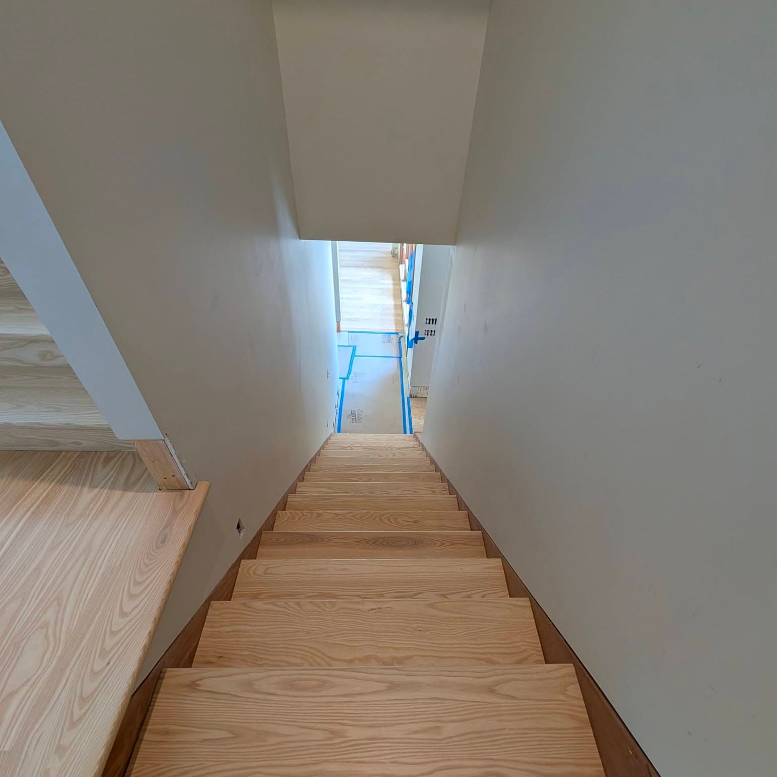 Looking down the same light wood stair run in a narrow hall