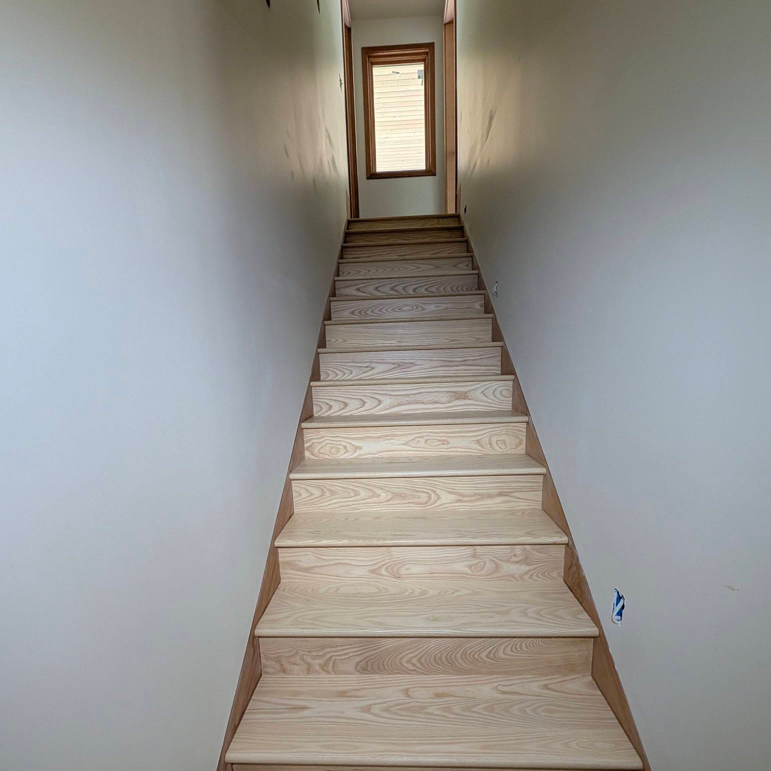 Looking up a straight light wood stair through a narrow corridor
