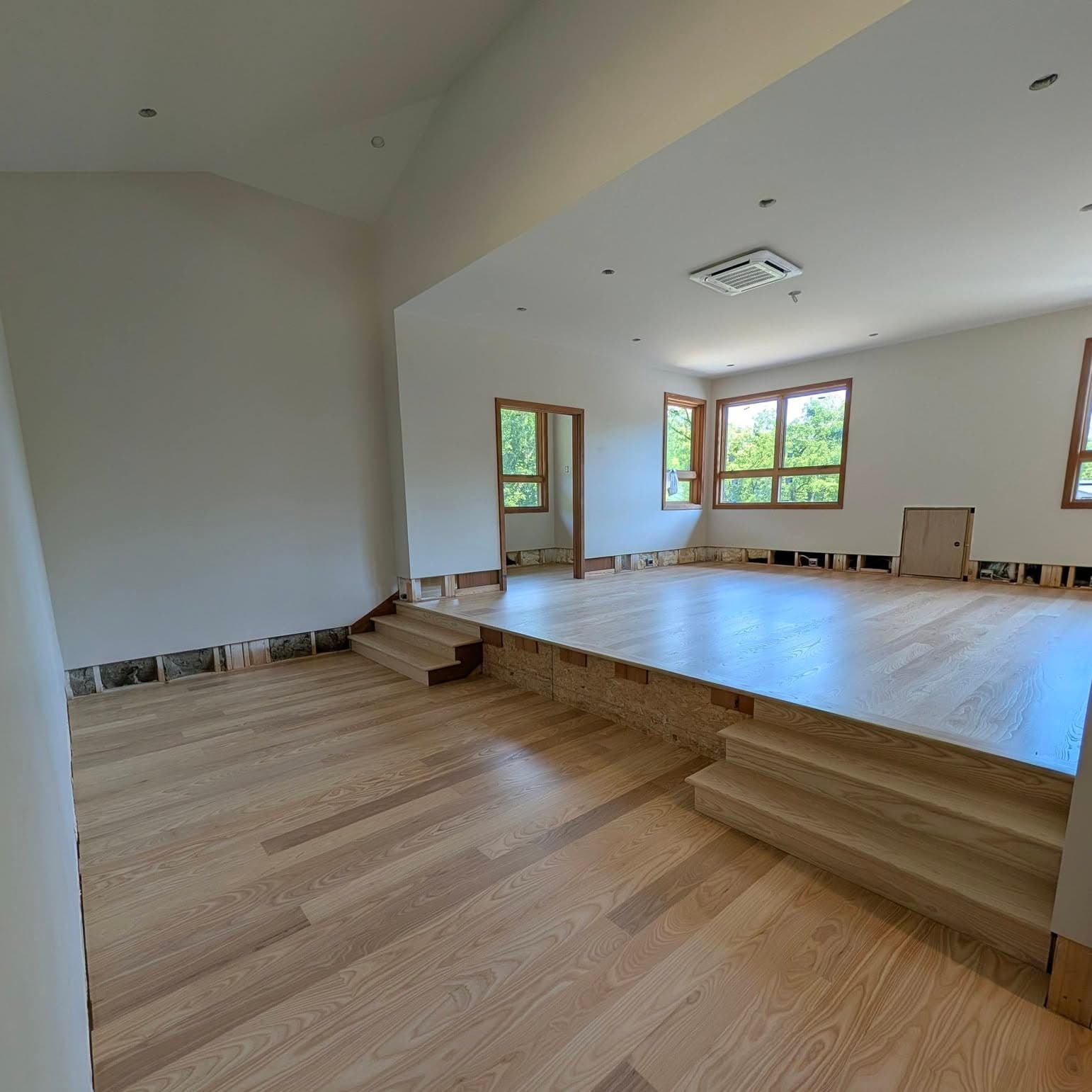 Split-level room with two short three-step hardwood stairs to a raised platform