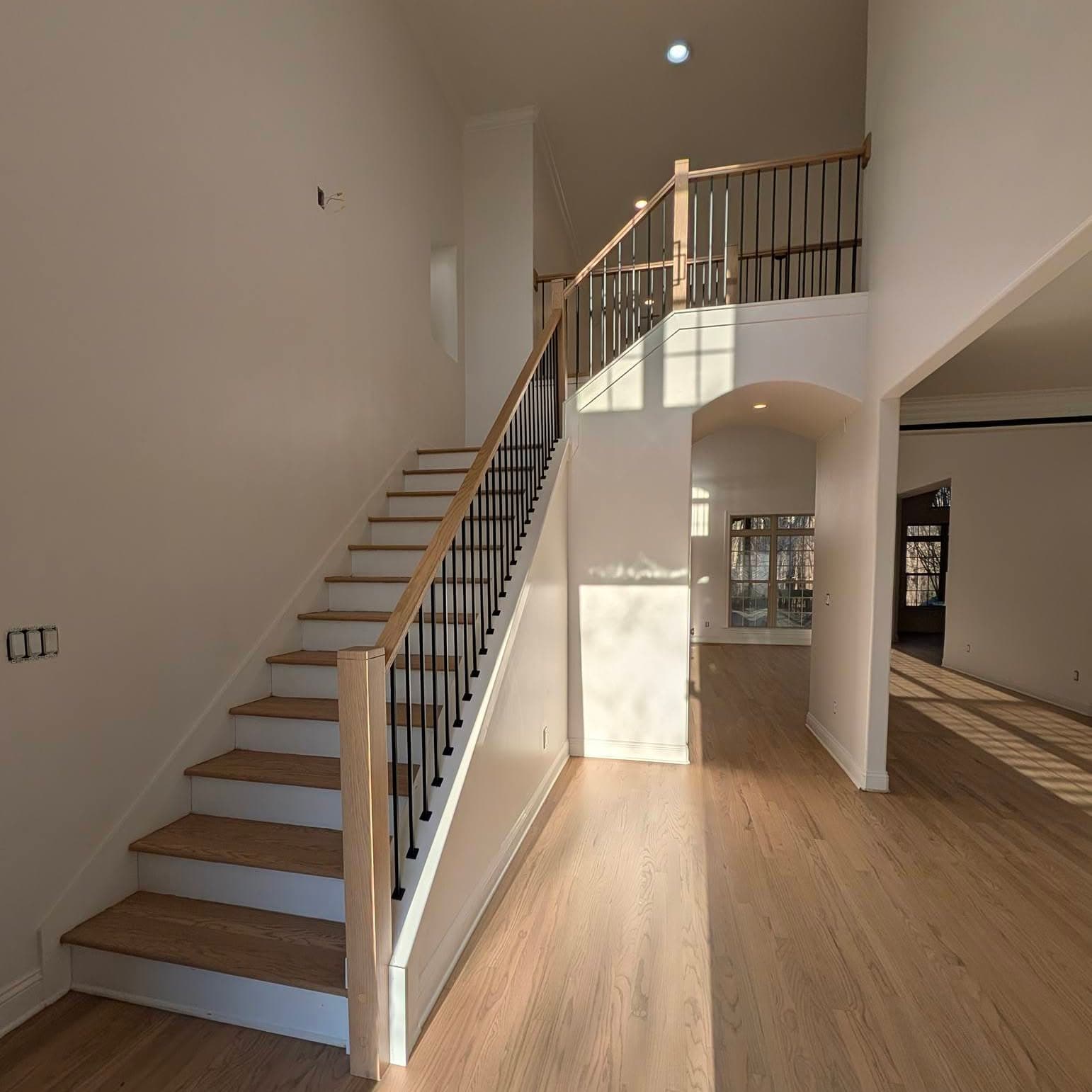 Stair with light wood treads, white risers, black metal balusters and wood handrail