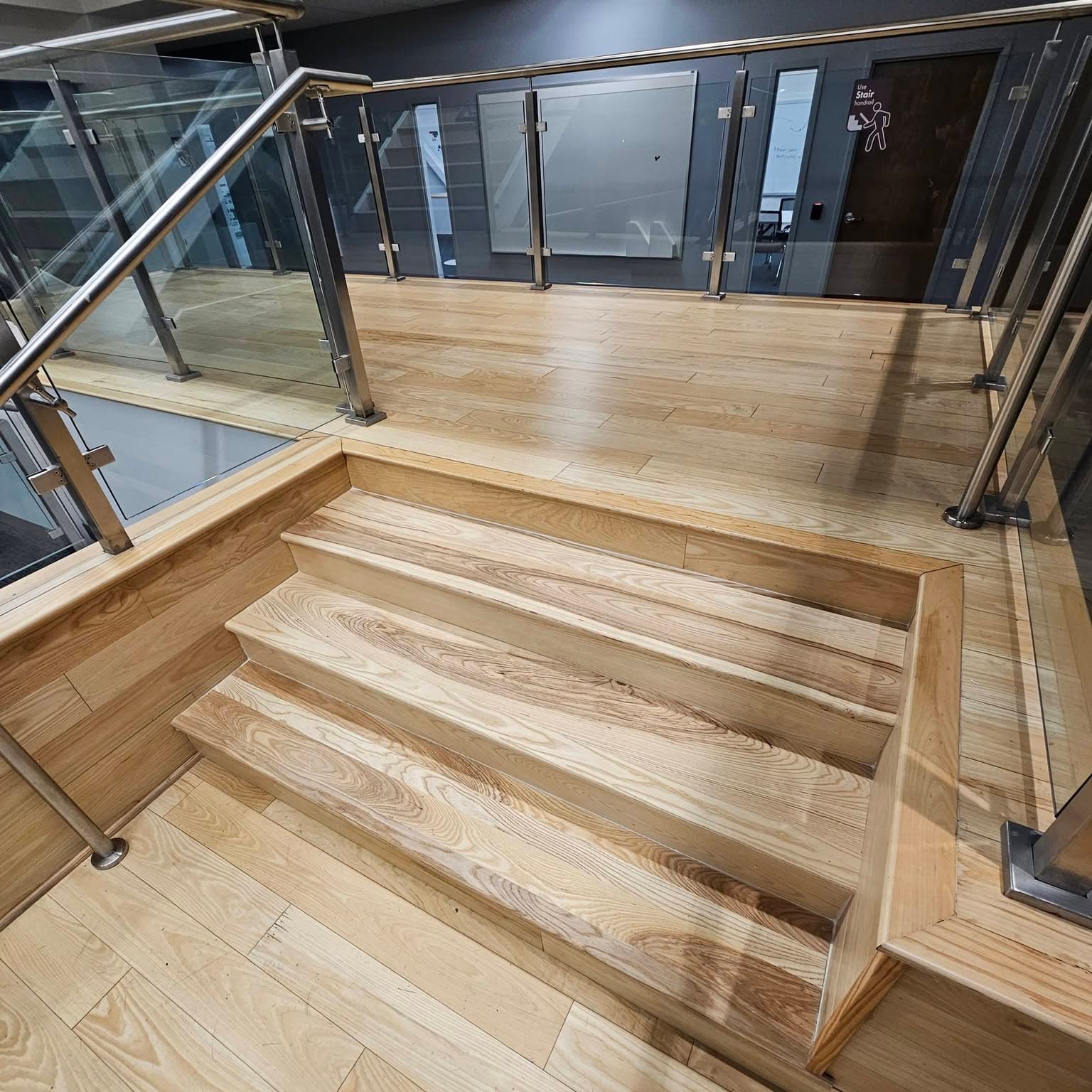 Top of a light wood stair landing with glass and metal railings