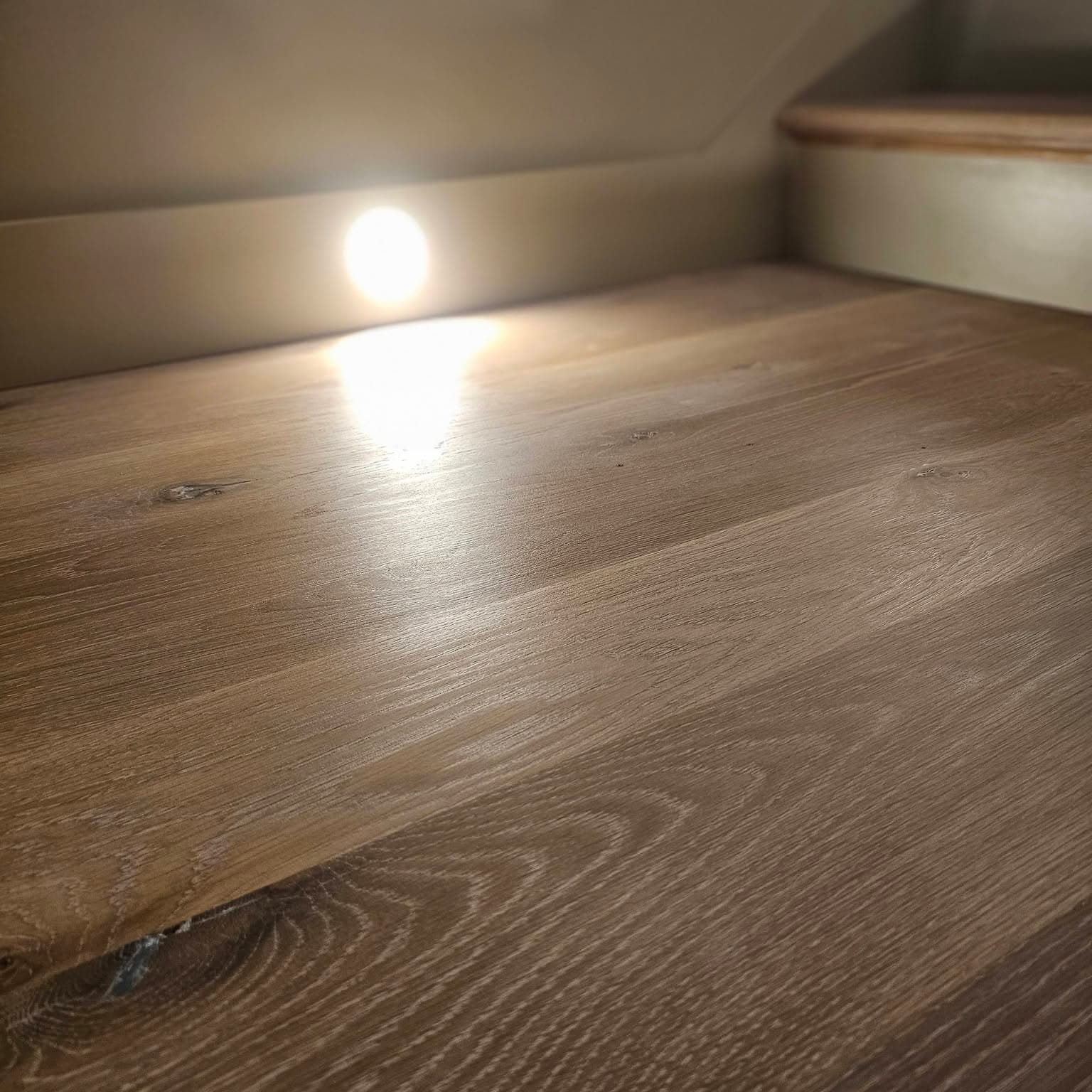 Close-up of a light wood tread with a circular step light in the riser