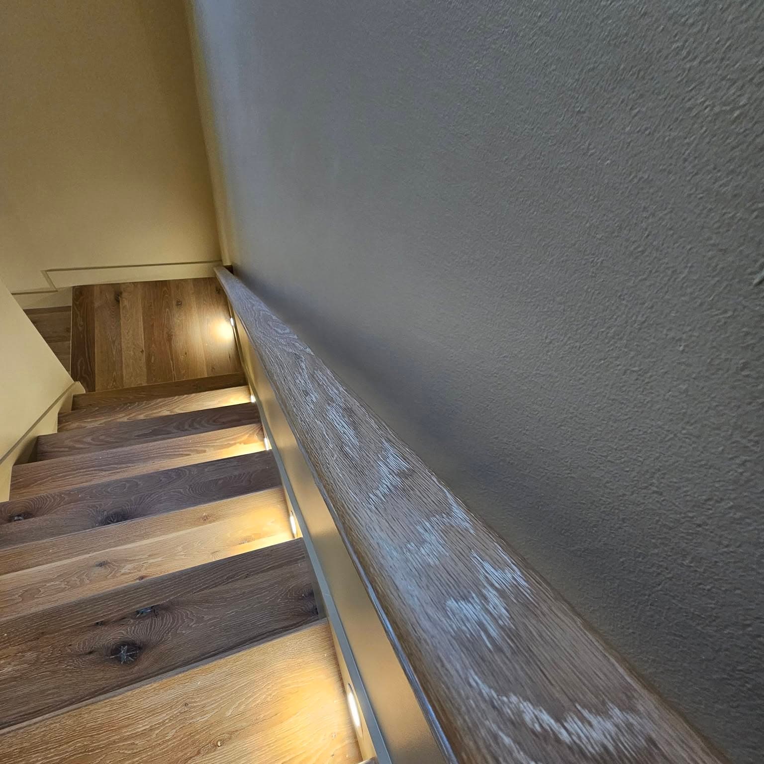 Looking down a dark wood stair with warm circular lights in the stringer