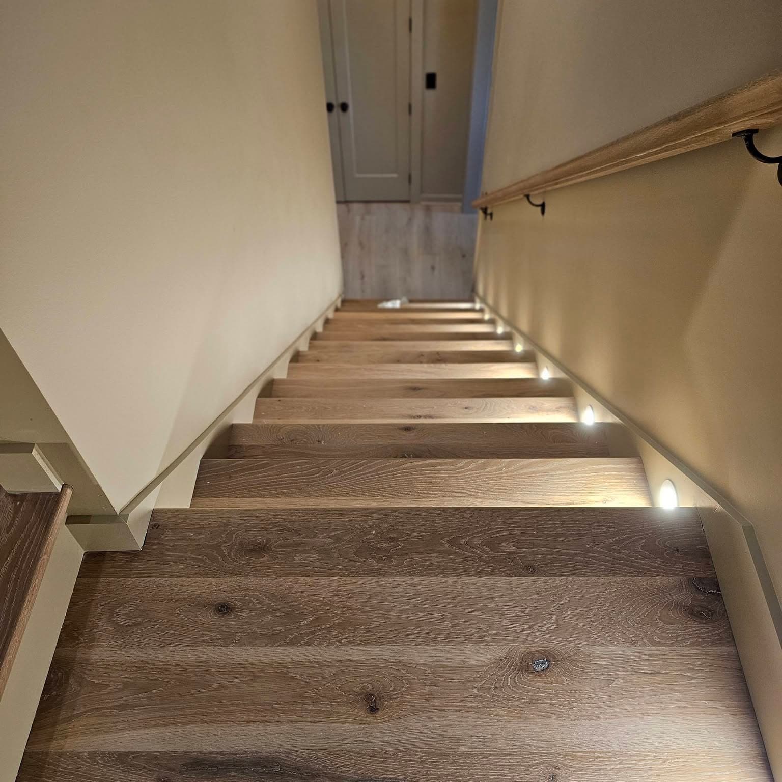 Downward view of a dark wood stair with step lighting on the right