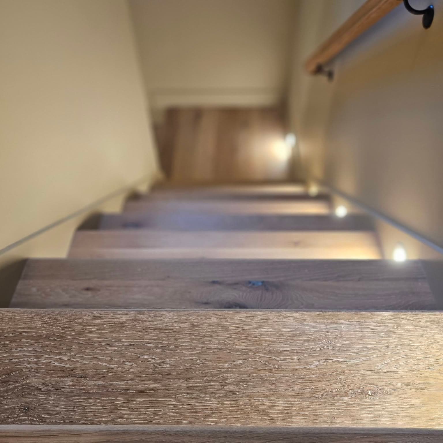 Another downward view of the same dark wood stairs with lights