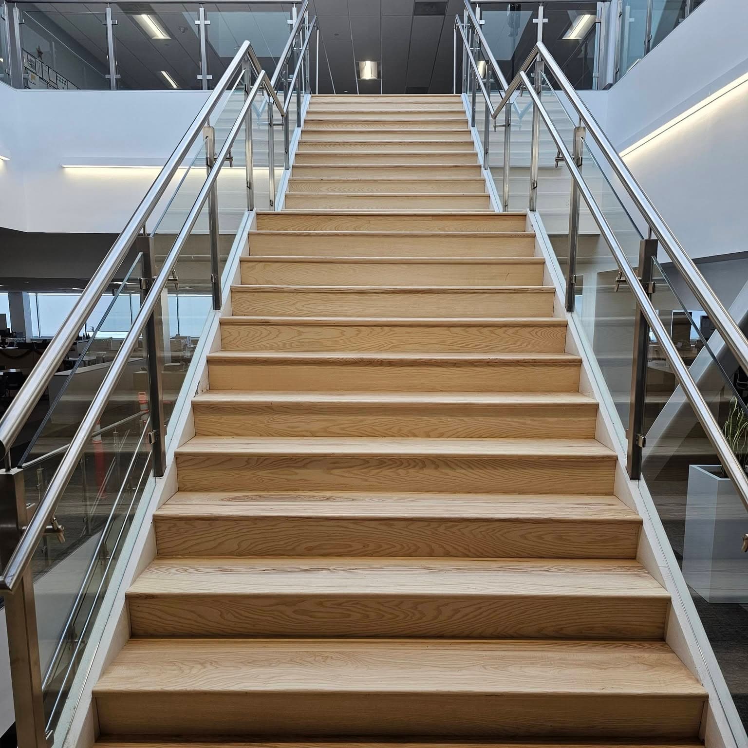 Looking up a long modern stair with light wood treads and metal handrails