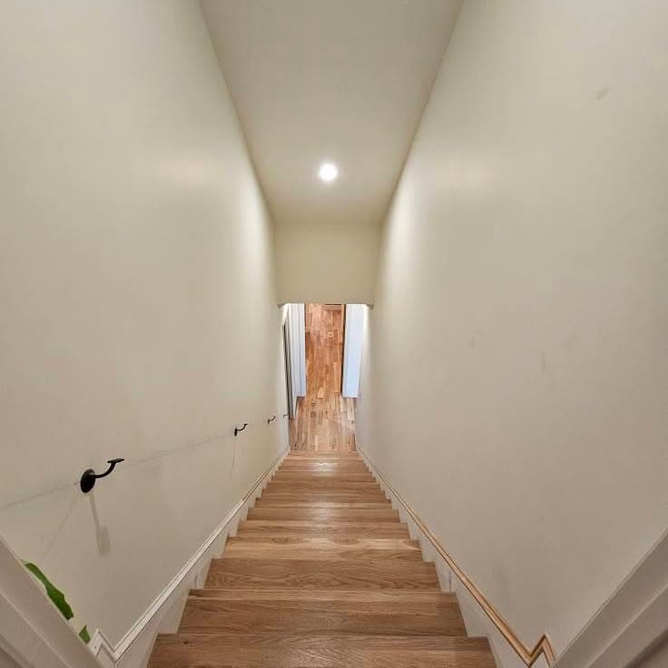 Looking down a wooden stair between two white walls
