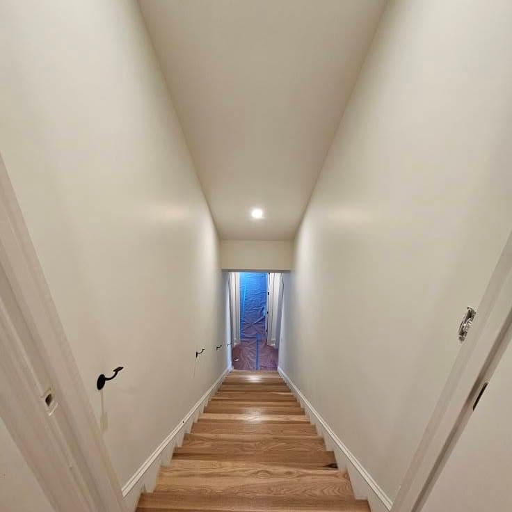 Similar top-down view of the same wooden stair between white walls