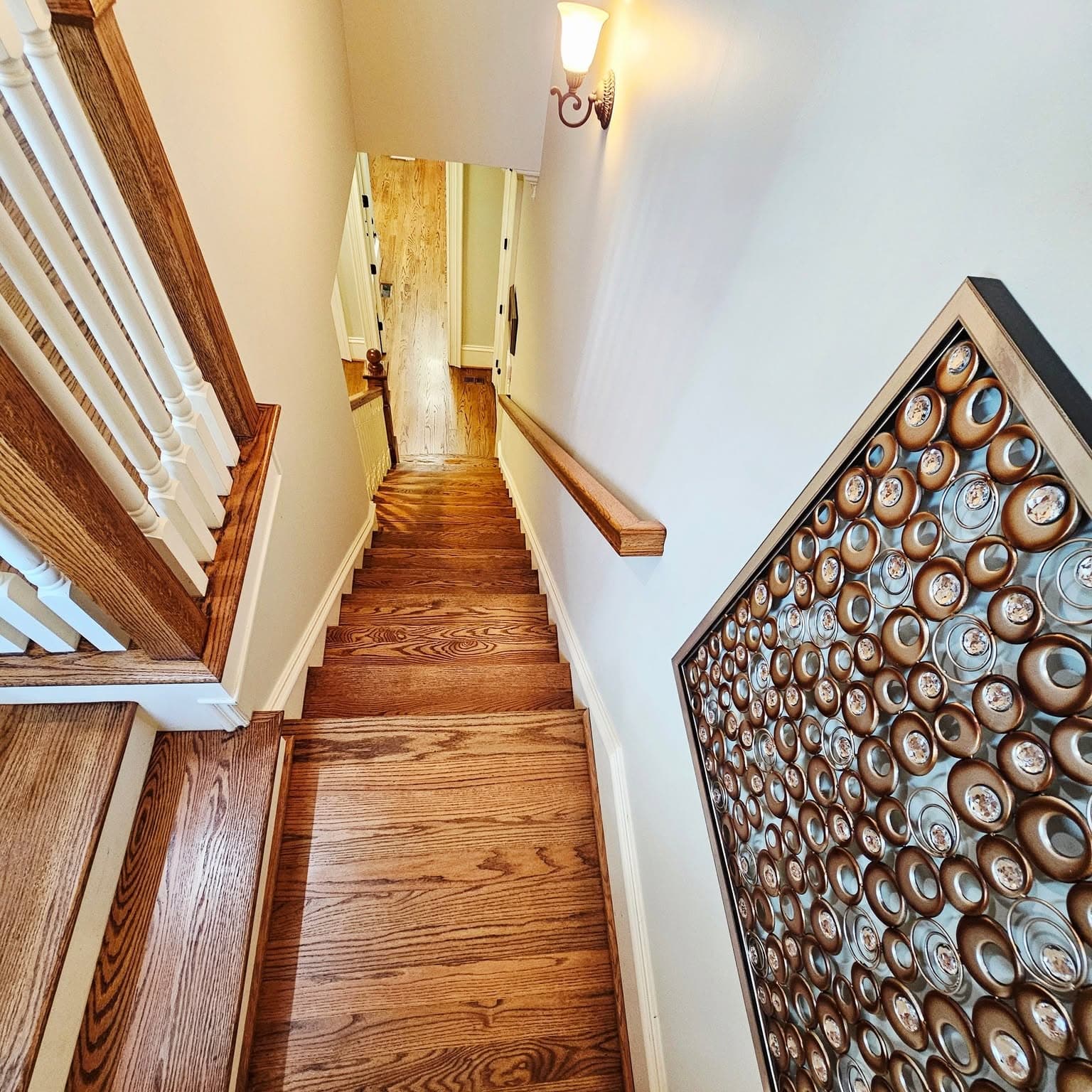 Looking down a straight wooden stair with white spindles and wood handrail