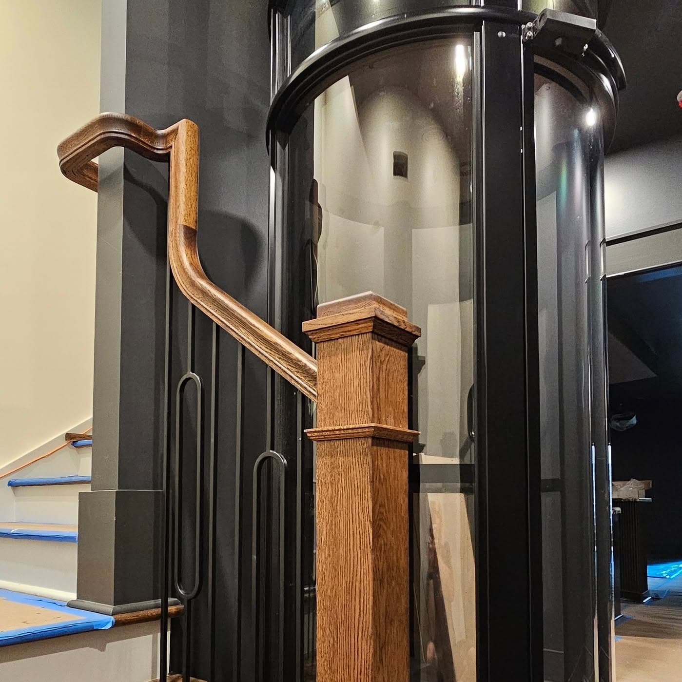 Wooden handrail and newel beside a dark cylindrical home elevator