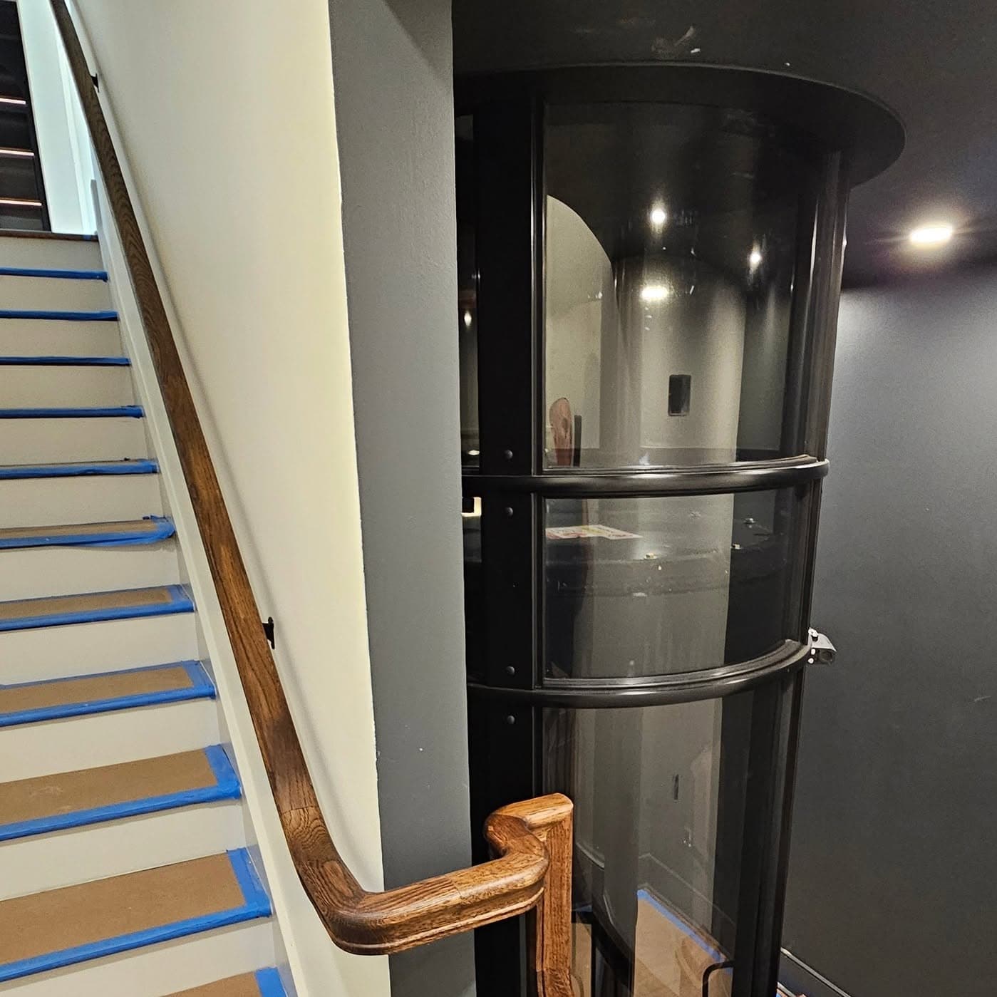Wooden stairs with blue painter's tape on tread edges beside an elevator shaft