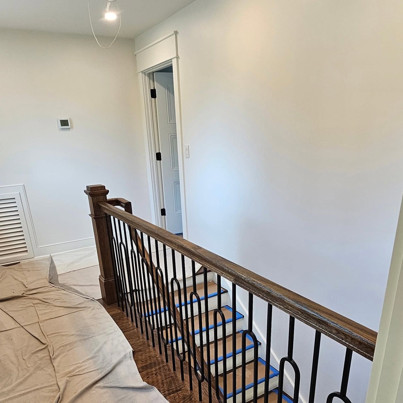 Top of a stair with ornate dark metal balusters, wood handrail, and taped treads