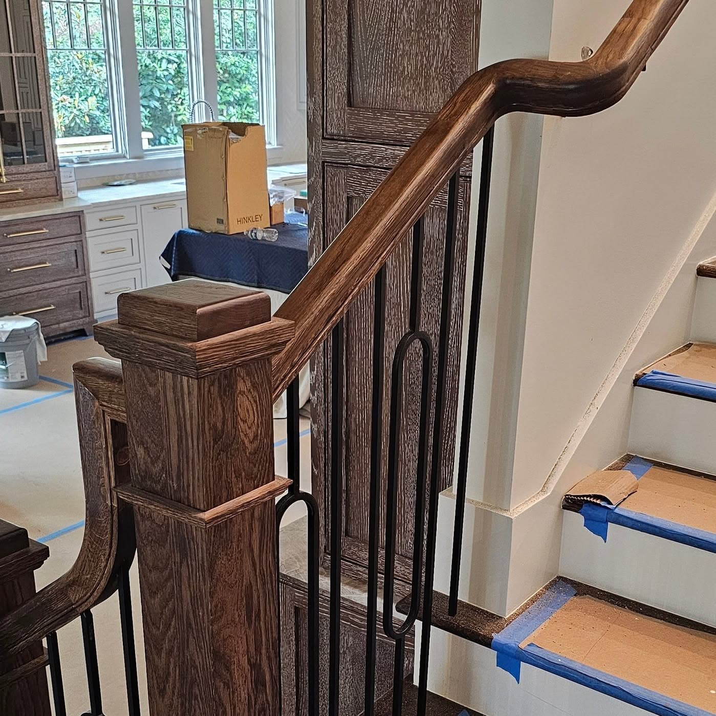 Close view of a wooden newel and handrail start; blue tape on treads