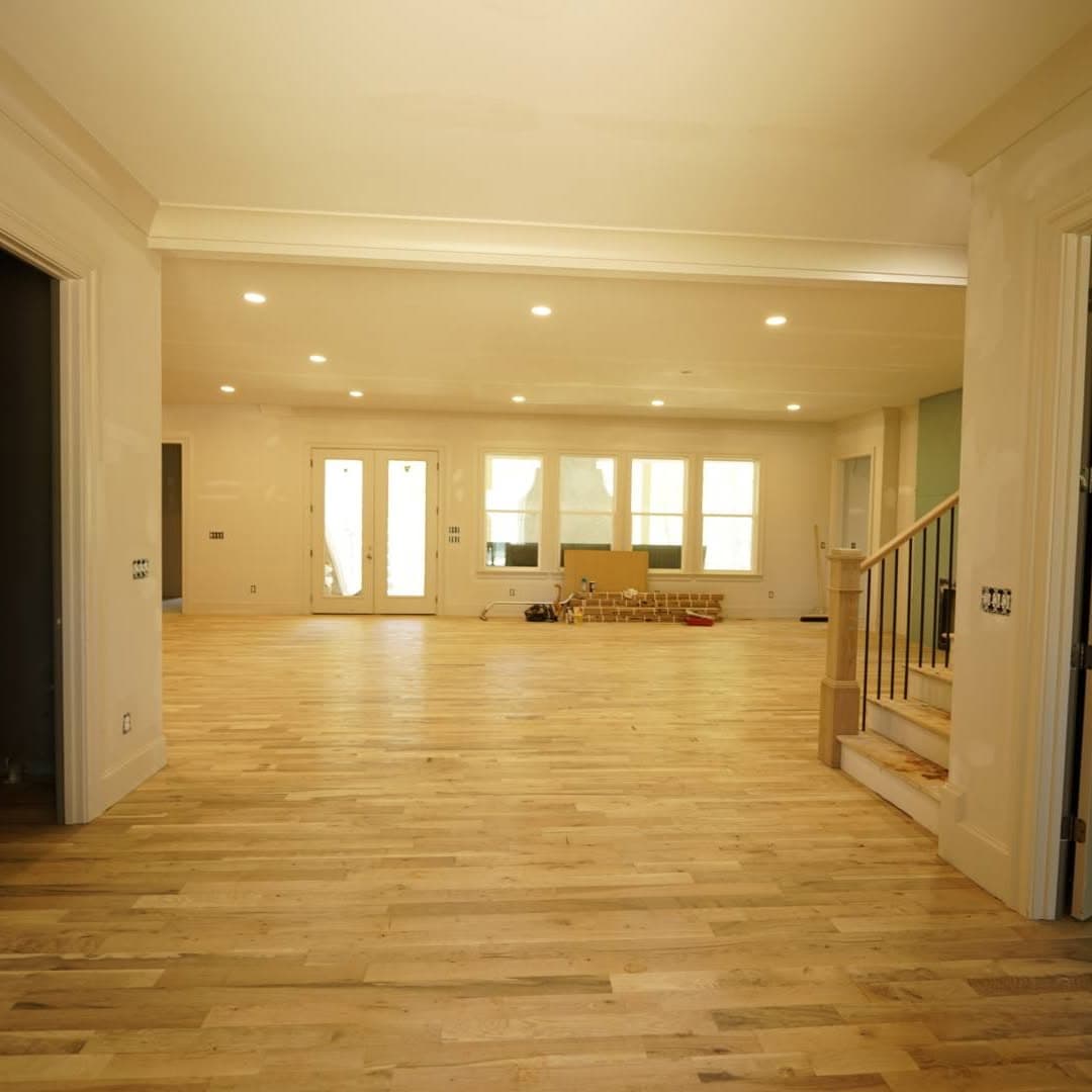 Large room with new light hardwood; stair at right with black spindles and wood newel