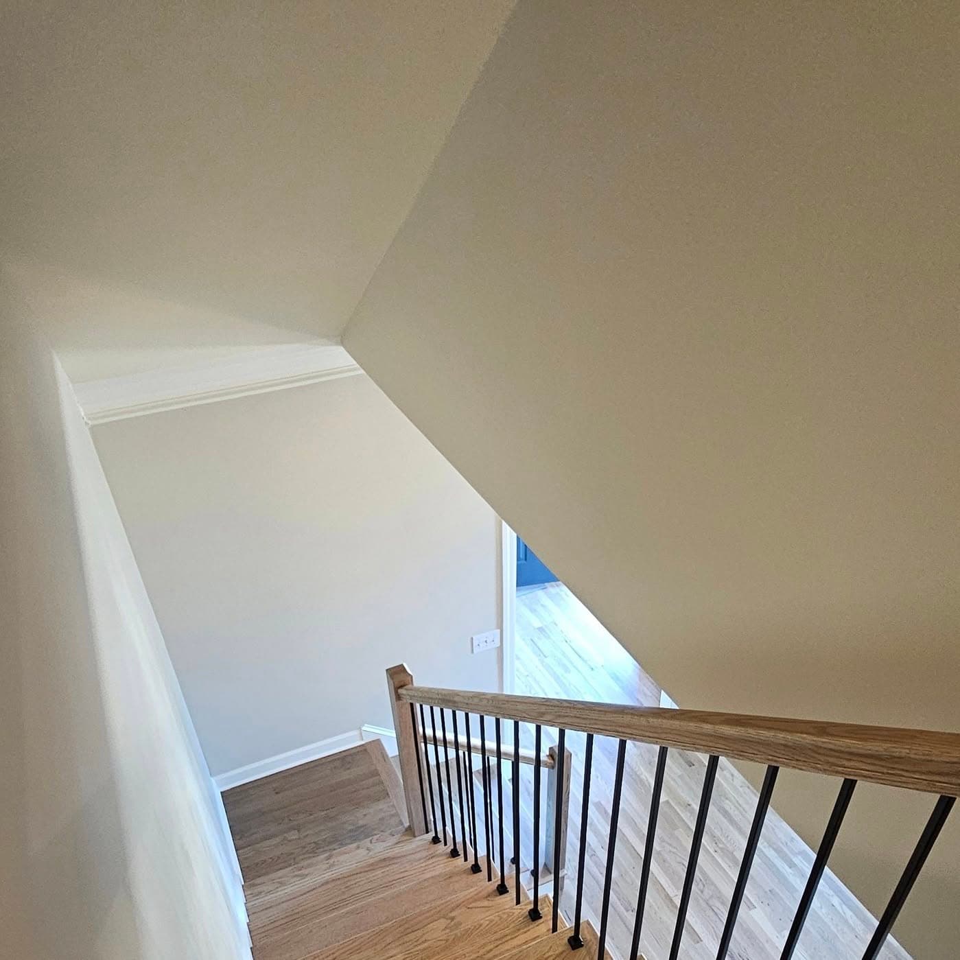 Looking down light wood treads, white risers, black metal balusters and wood cap