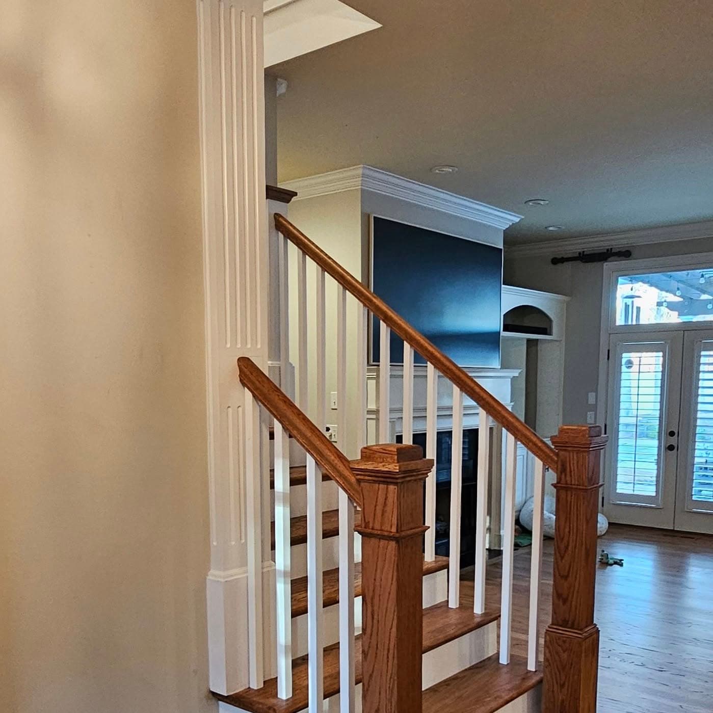 Section of wood stair railing with white spindles beside a dark pillar