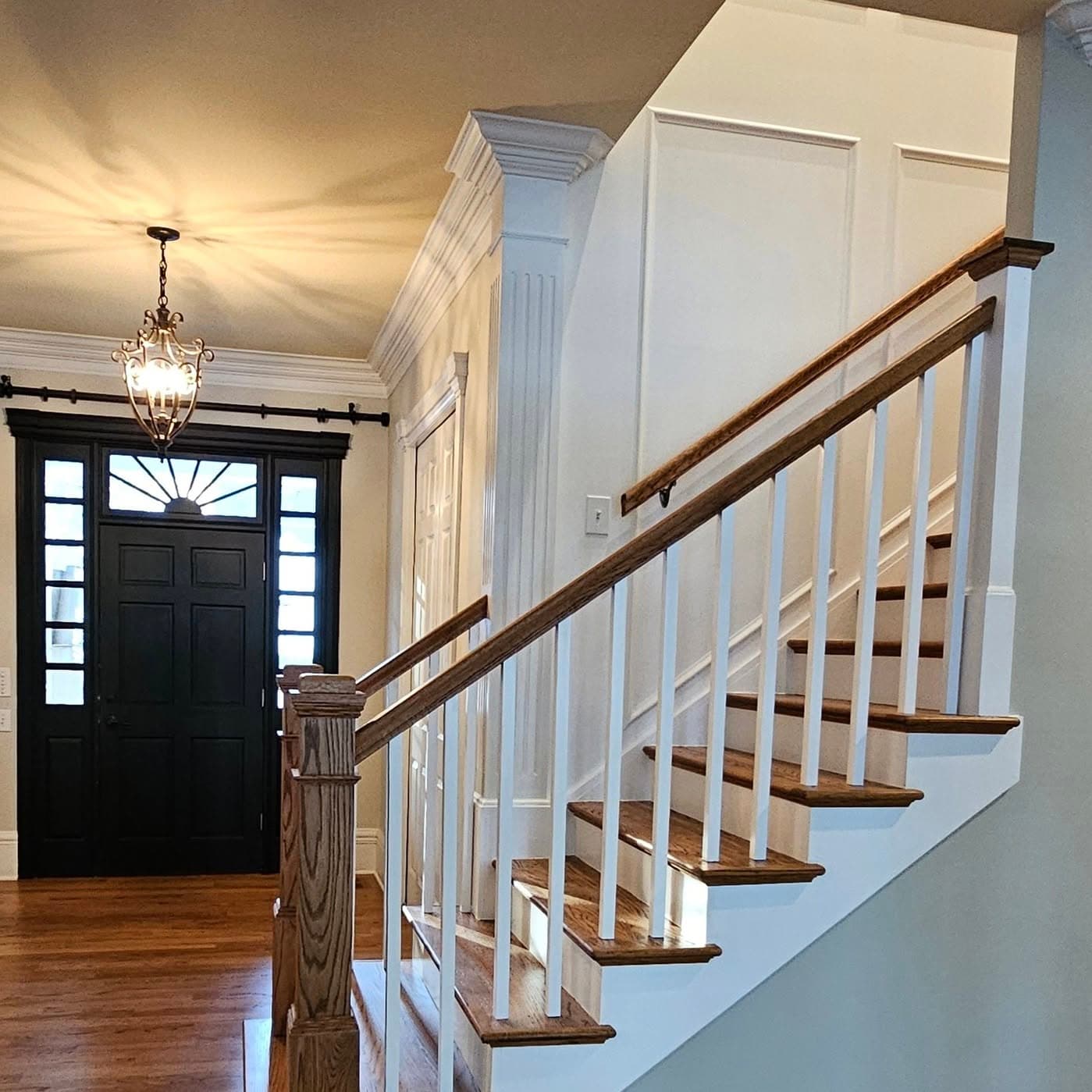 Stair base near an entry door with a prominent wooden newel and white spindles