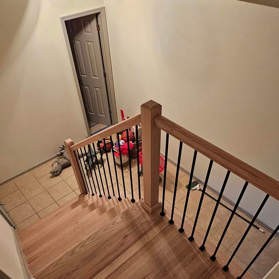 Looking down a stair with light wood handrail and black metal spindles