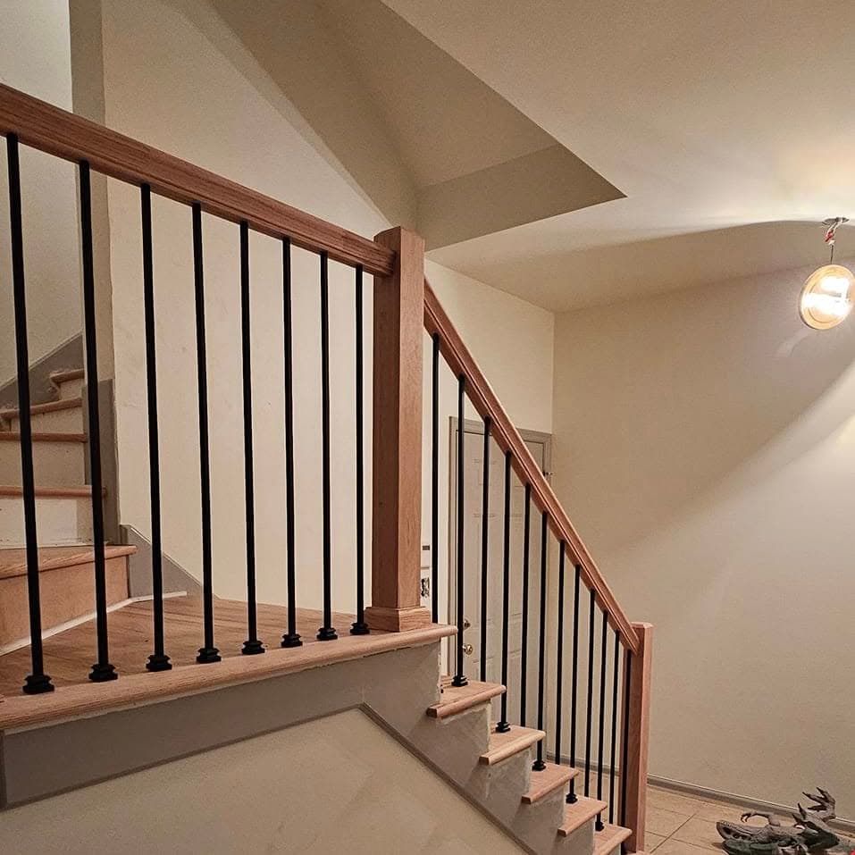 Looking up a short stair with light wood treads, handrail, and black spindles