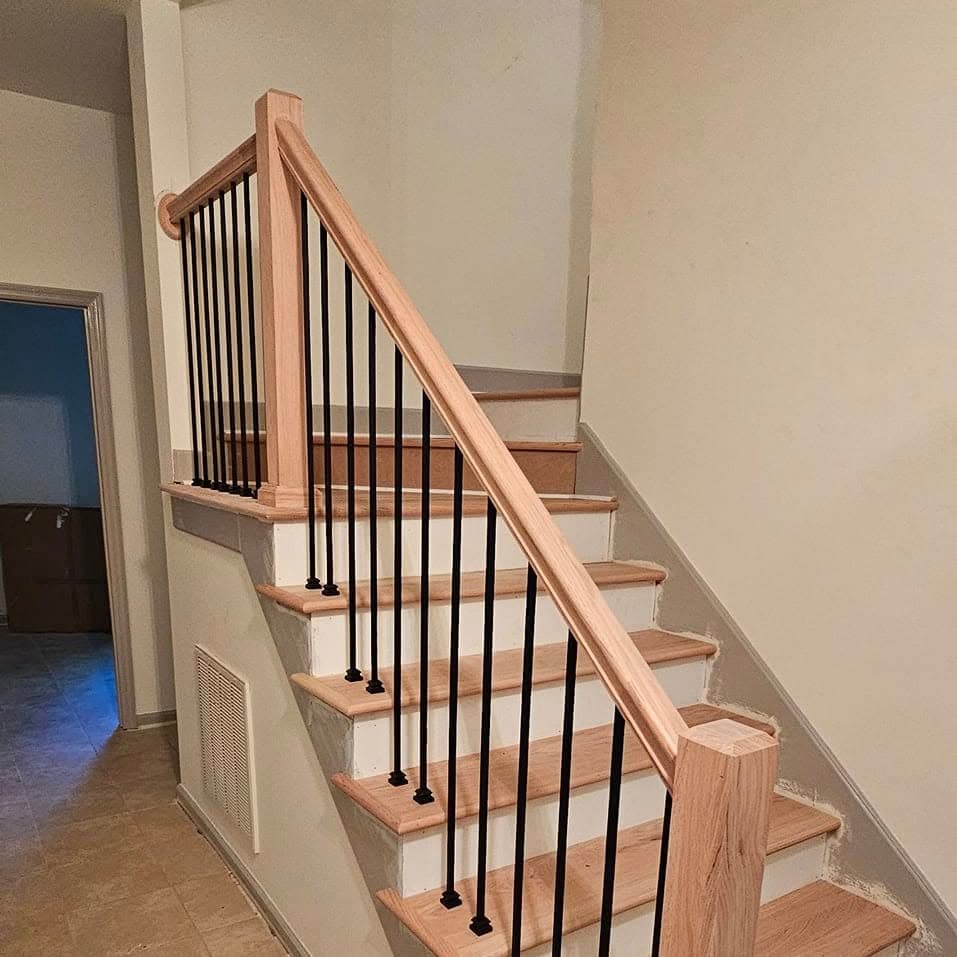 From the bottom looking up light wood steps and black-spindle railing