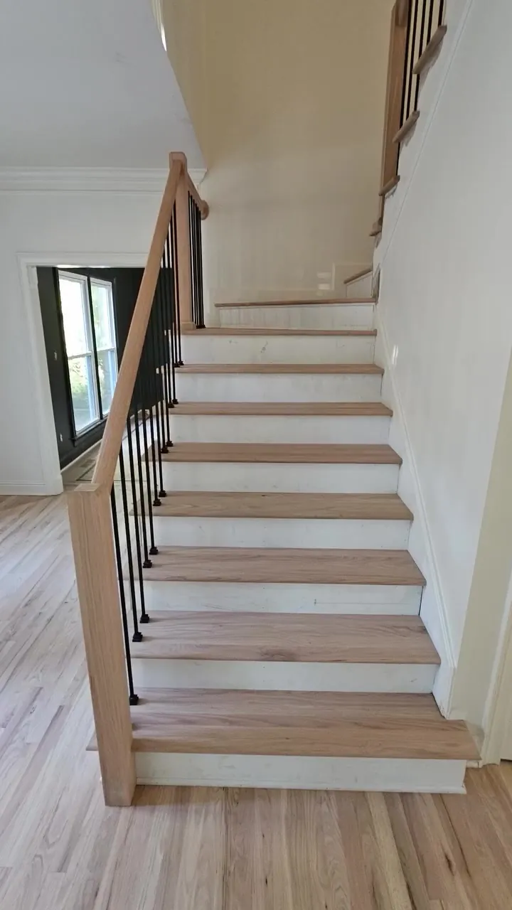 After: light oak treads, white risers, a square wood newel, and matte black balusters on a Huntsville carpet-to-hardwood stair