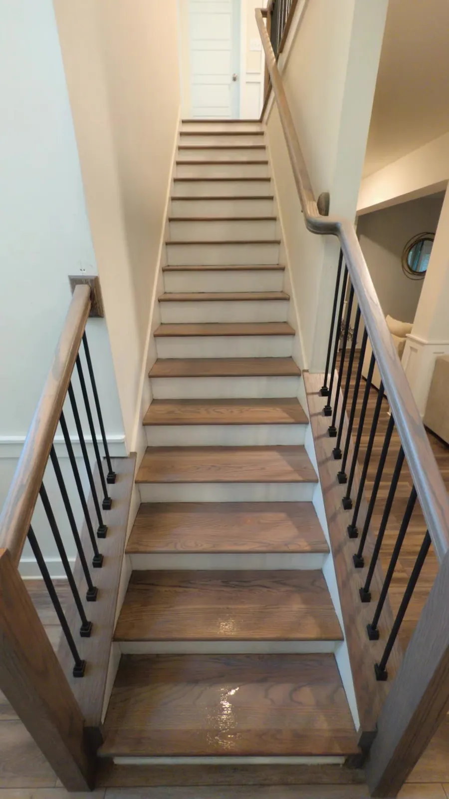 Looking down oak stair treads with white risers, a wood handrail, and matte black balusters after a Madison railing replacement by Rocket City Stairs