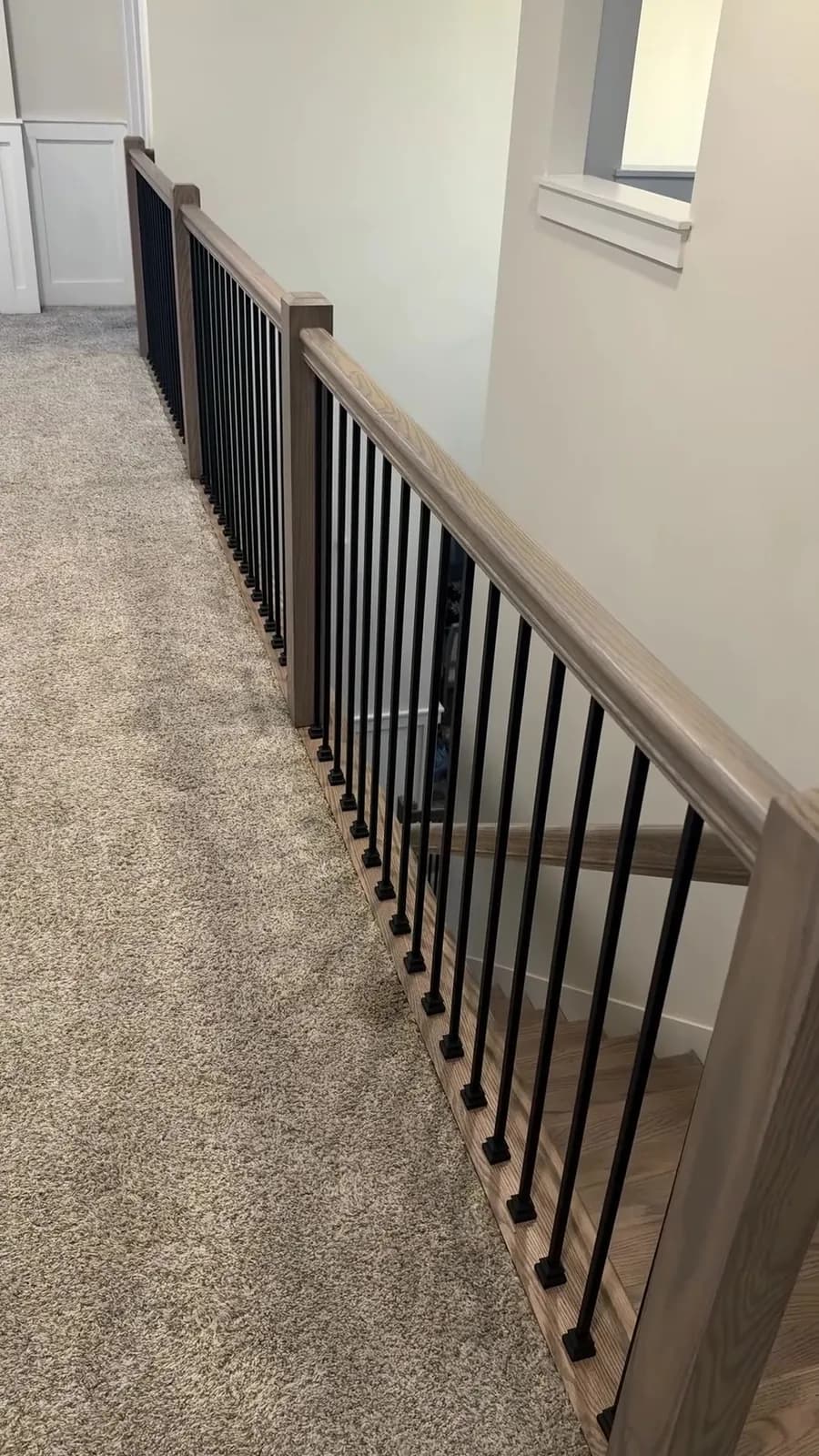 Upper landing oak cap, square newel, and matte black balusters over hall carpet after a Madison stair railing replacement