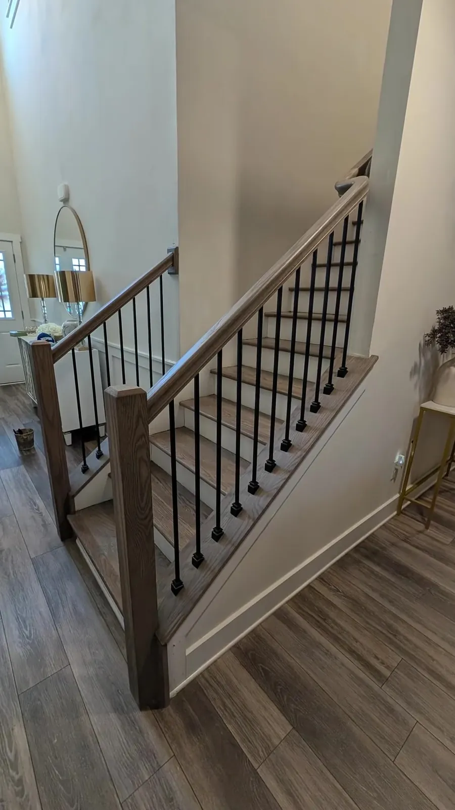 Square oak newel at the base of oak treads and white risers with matte black balusters meeting a gray plank foyer in Madison