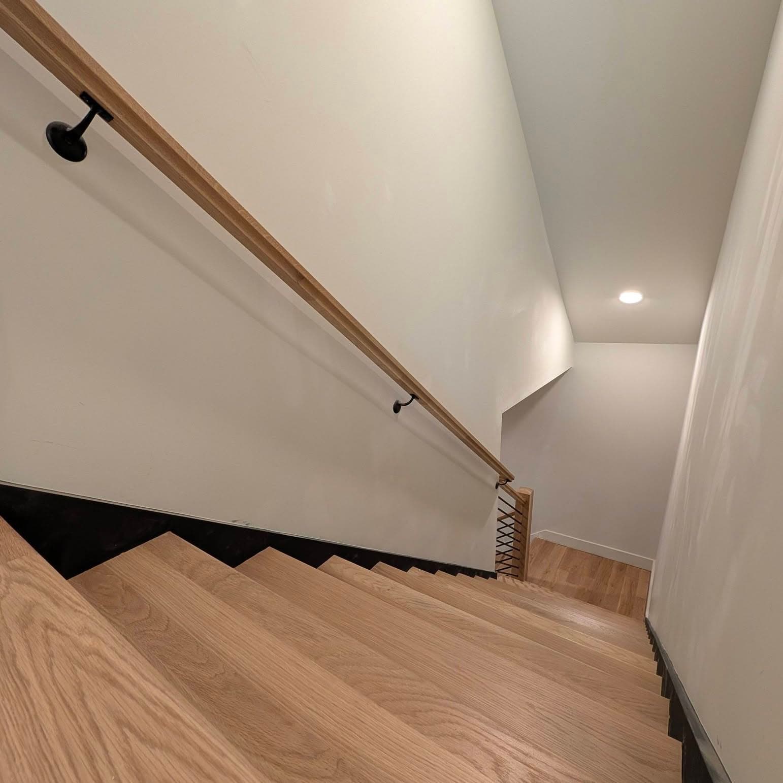 Interior stair with light oak treads, dark risers, and a black metal handrail in Huntsville, Rocket City Stairs